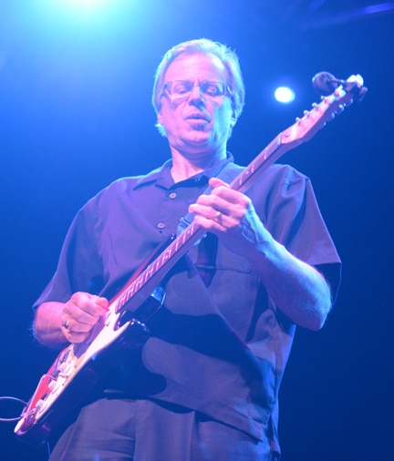 Joe Scott playing guitar on stage with his band.